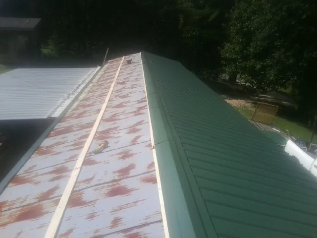 Old rusted panels beside newly installed green metal roofing — Wind Damage Roof Repair by Roofing Brothers in Brewster